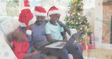Dizüstü bilgisayar kullanarak gülen aile ve Noel Baba şapkalarının üzerine yağan kar animasyonu. Noel, kış, gelenek ve kutlama konsepti dijital olarak oluşturulmuş video.