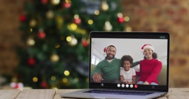 Bilgisayar başında Noel Baba şapkası takan mutlu bir aile. Noel süslemeleri ve ağacı da var. Noel, şenlik ve iletişim teknolojisi dijital kompozit video.