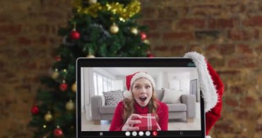 Bilgisayarda, Noel süsleri ve ağacıyla görüntülü konuşan mutlu beyaz kadın. Noel, şenlik ve iletişim teknolojisi dijital kompozit video.