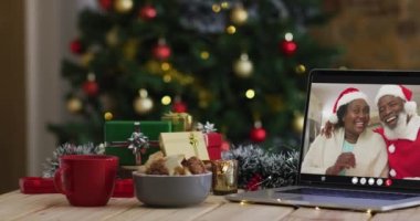 Laptop 'ta Noel Baba şapkası takan Afrikalı son sınıf öğrencisi çiftin Noel ağacı var. Noel, şenlik ve iletişim teknolojisi dijital kompozit video.