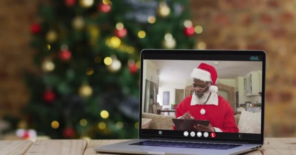 穿着圣塔服装的资深非洲裔美国人在笔记本电脑上通过视频通话 还带着圣诞树 节日和通信技术数码合成录像 — 图库视频影像