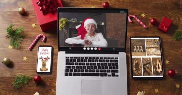 在笔记本电脑上戴着圣诞礼帽的白人女性 带着智能手机 平板电脑和装饰品 节日和通信技术数码合成录像 — 图库视频影像