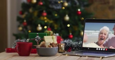 Kafkasyalı son sınıf çifti dizüstü bilgisayarda Noel ağacıyla el sallıyor. Noel, şenlik ve iletişim teknolojisi dijital kompozit video.