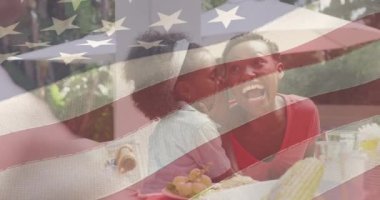 Afro-Amerikan ailesinin yemek yiyip gülümsemesi üzerine Amerikan bayrağının animasyonu. Vatanseverlik ve kutlama konsepti dijital olarak oluşturulmuş video.
