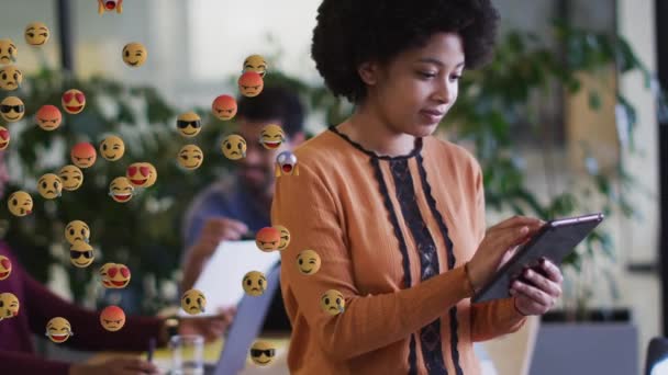 Animação de ícones de emoji digitais sobre sorrir mulher de negócios de raça mista usando tablet — Vídeo de Stock