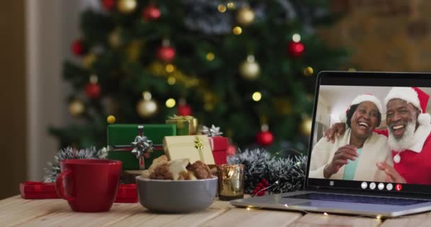 非洲裔美国老年夫妇在笔记本电脑上戴着圣诞帽 带着圣诞圣诞树 带着圣诞礼帽 节日和通信技术数码合成录像 — 图库视频影像