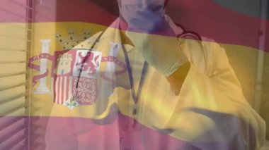 Yüz maskesi takan doktorun üzerinde sallanan İspanya bayrağının animasyonu. küresel tıp, covid 19 pandemik konsept sırasında sağlık hizmetleri dijital olarak üretilen video.