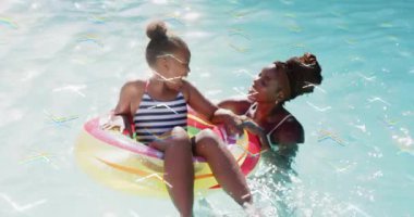 Anne, kızlarının suya tekme atması gibi gökkuşağı halkalarını sabitliyor, yüzme derslerine güven katıyor. Aile, su oyunu, su sporu, eğlence, eğlence, modern, canlı