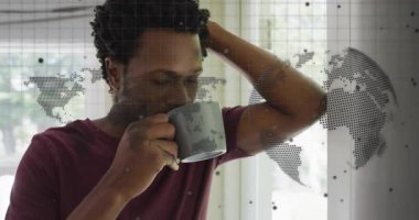 Adam içkisini yudumlarken gri bardağı kaldırıyor ve teknoloji vitrininde animasyon dünya haritasını aktifleştiriyor. Düşünce, rahatlama, farkındalık, küresel bağlantı, modern yaşam tarzı, iç tasarım