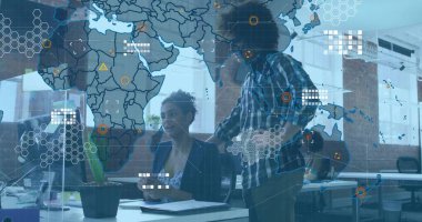 Dijital dünya haritasını inceleyen iki meslektaş açık planlı ofis masasında, masaüstü monitörüyle örtüşüyor. İşbirliği, takım çalışması, yenilik, teknoloji, veri, çalışma alanı, modern