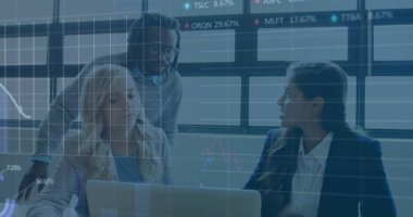 Takım elbiseli üç profesyonel ofiste dizüstü bilgisayarın etrafında toplanıyor ve monitörler hisse senedi verilerini gösteriyor. İşbirliği, analitik, teknoloji, finans, şirket, takım çalışması, yenilik