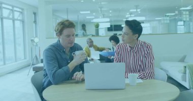 Modern ofiste elinde kupa olan ve gümüş dizüstü bilgisayarda beyaz kupalarla yazı yazan iş arkadaşları. İşbirliği, takım çalışması, modernlik, açık alan, yenilik, üretkenlik, profesyonellik