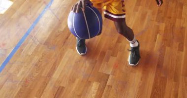 Genç çocuk spor salonunda çömelmiş, topa bastırıyor spor eğitimi için top sürme talimi yapıyor. Sporcu, antrenman, aksiyon, hareket, pratik, spor, spor