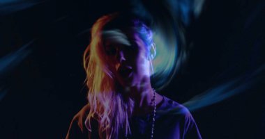 Dönen mor ve yeşil projeksiyonlar. Karanlık stüdyoda, kulaklıkları ve kolyesi olan bir kadını aydınlatıyor. Soyut, enerjik, fütüristik, dijital sanat, gece hayatı, yaratıcı, ruh hali