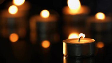 Lens alevi kehribar bokeh boyunca süzülürken mum alevi masa ısıtma sahnesinde yanıp sönüyor. Çevresel, samimi, sıcak, yansıtıcı, romantik, minimalizm, sükunet