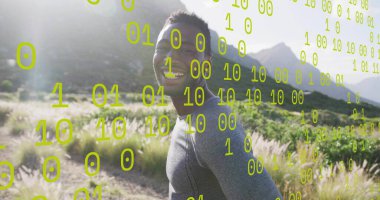 Gülümseyen koşucu gri atletik üstte ayakta duruyor çimenli ovada sola döndü, ikili kod örtüsüyle. Spor giysileri, açık hava, dijital, teknoloji, doğa, canlılık, fitness