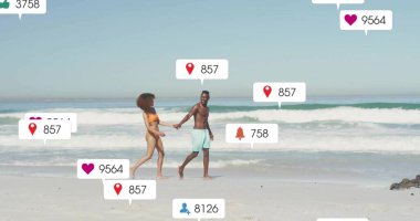 Sahil şeridinde turuncu bikini ve deniz mavisi şort giyen ve yüzen uyarı simgeleri olan yürüyen bir çift. Romantik, boş zaman, tatil, açık hava, canlı, yaşam tarzı, bağlantı