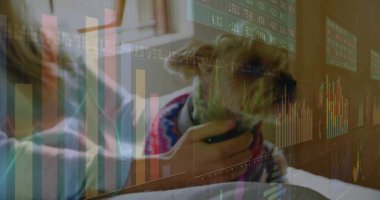 Oturan kadın süveter giyiyor, kulaklık takıyor. Ev masasında, pencere kenarında yüzen borsa verileri olan kulaklık takıyor. Teknoloji, finans, uzaktan çalışma, dijital, modern, üretkenlik, gündelik