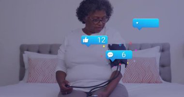 Üst düzey kadın kelepçeleri paketliyor ve ampulleri pompalıyor. Yatağın üstünde canlandırılmış sağlık gelişimi ikonları oluşturuyor. Geriatrik, sağlık, sağlık denetimi, dijital arayüz, ev bakımı, otomasyon, dinginlik