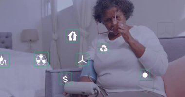 Kıdemli kadın yüzen sağlık simgelerini fark ediyor, kelepçe takıyor, gözlük kaldırıyor ve monitörleri inceliyor. Yaşlılık, sağlık, dijital, ev, tefekkür, tıbbi, teknoloji