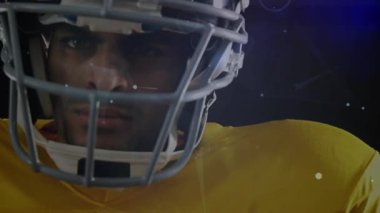 Futbolcu kameraya bakıyor ve kask çevresindeki parçacıklardan oluşan bir hale oluşturuyor. Spor aletlerini gösteriyor. Sporcu, dijital, gelecekçi, yenilik, teknoloji, enerji, hareket