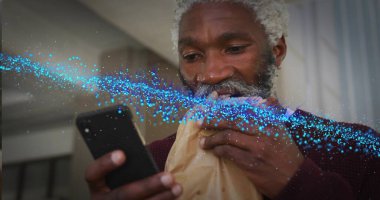 Ev mutfağında akıllı telefon tutan kıdemli bir adamı, kahverengi çantalı pasta ve mavi dijital akımla ısırmak. Teknoloji, yaşam tarzı, modern, aşçı, gündelik, canlı, bağlantı