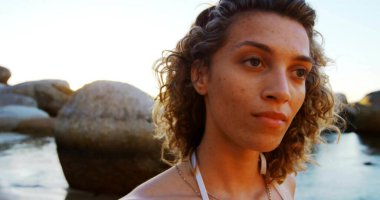 Gün batımında kıyıda üzerinde kayalar olan ince askılı mayo ve zincirli kolye giyen bir kadın. Manzara, doğal, sakin, alacakaranlık, kıyı, meditasyon, minimalist