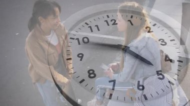 Saati 20 dakika olarak gösteren açık bir saat altında, telefonları kaydırarak sosyal medyayı paylaşan iki arkadaşı selamlamak. Gündelik, arkadaşlık, bağlantı, gençlik, açık hava, iletişim, yaşam tarzı