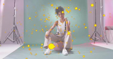 Model üzerinde sürüklenen hareketli sarı parçacıklar kayışları ayarlıyor, moda çekimi için poz veriyor. Stüdyo, moda, minimalizm, cazibe, güzellik, zarafet, modern