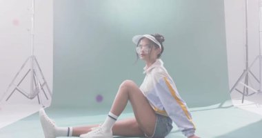 Yeşil sette oturan manken başını çevirip sürüklenen renkli parçacıklara ve yol göstericiliğe sebep oluyor. Stüdyo, moda, zarafet, minimalizm, yaratıcılık, hareket, çağdaş