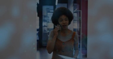 Ofiste elinde akıllı telefon ve kağıtlarla paslı elbise giyen bir ofis çalışanı konuşuyor. Cam bölmeler var. Profesyonel, kentsel, minimalist, kurumsal, gösterişli, iletişim, işyeri