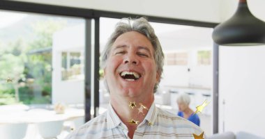 Çizgili tişörtlü gülümseyen erkek, açık planlı bir evde, sürgülü cam kapılar ve kolye lamba ile poz veriyor. Aile, yaşam tarzı, modern, iç mekan, dinginlik, bağlantı, sıcaklık