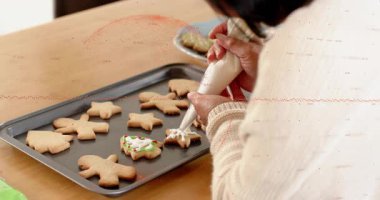 Ev yapımı fırıncı beyaz krema sıkıyor, kar tanesi sıkıyor sonra da bayram kurabiyesi sanatı için kırmızıya geçiyor. Şenlikli, işçilik, gelenek, el yapımı, mevsimlik, rahat, ayrıntılı