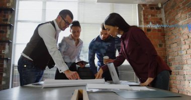 Dizüstü bilgisayar ve tabletle çatı katındaki planların üzerine eğilmiş iş gündelik profesyonellerini inceliyorum. İşbirliği, takım çalışması, kentsel, modern, beyin fırtınası, tasarım, yenilik