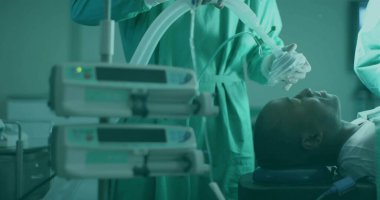 Ameliyathanedeki hastaya anestezi maskesi takan önlüklü anestezi uzmanı. İnfüzyon pompalarıyla, fotokopi odasıyla. Tıbbi, sağlık, cerrahi, ameliyat, hastane, steril, prosedür