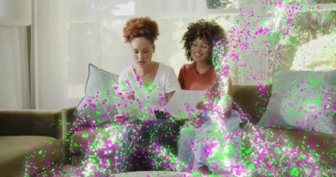 İki kadın kanepede yüksek sesle kitap okuyup içeriği gözden geçirmek için metni işaret ediyor ve kağıtları değiştiriyor. İşbirliği, dostluk, rahatlama, ev ofisi, günlük tarz, neşeli, iletişim