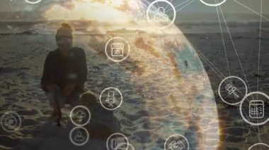 Kum kepçelemeye ve günbatımında veri küresi oluşturan teknoloji ikonlarına yol gösteren bir kadın. Aile, teknoloji, yenilik, dijital, açık hava, günbatımı, bağlantı