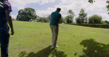 Yaşlı golfçü golf sahasında öne çıkıyor, topu yeşile doğru sürerken demir vuruşu yapıyor. Atletik, açık hava, spor, eğlence, takım çalışması, boş zaman, canlı