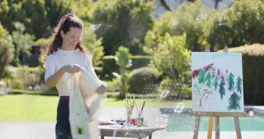 Ressam arka bahçedeki havuzda boya lekeli önlüğe uzanıyor önlük giyiyor ve fırça darbesi planlıyor. Sanat, manzara, boş zaman, açık hava, yaratıcılık, rahatlama, renk