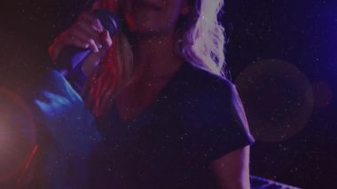 Kadın şarkıcı sahne ışıklarının altına giriyor, mikrofonu kavrayıp duygusal bir performans sergiliyor. Performans, vokal, konser, eğlence, sanatsal, sahne, anlamlı