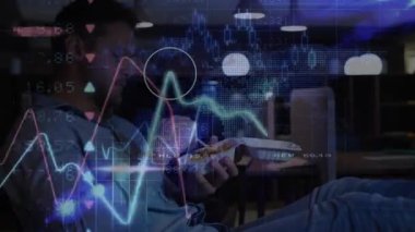 Paket servisi yapan, ısırığı kaldıran, dinlenme odası manzarasını kaplayan finansal tabloları izleyen bir adam. Teknoloji, finans, veri görselleştirme, modern, gündelik, çalışma alanı, dijital