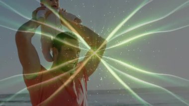 Sahilde kızını omuzlarına alan bir adam teknolojide parıldayan yeşil enerjiyle neşeyi paylaşıyor. Enerji, aile, bağlantı, ruhani, ışıltı, uyum, iyimserlik