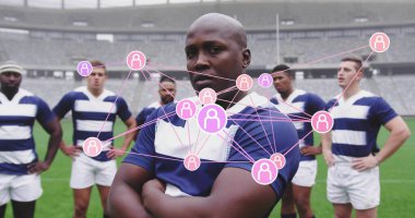Standing rugby player in striped jersey crossing arms on grass field at stadium, with node icons. Athletics, teamwork, collaboration, sportsmanship, competitive, energetic, digital