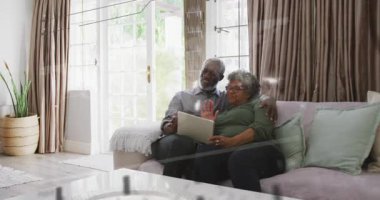 Kanepede elinde tablet olan olgun bir çift, teknisyen çift üzerinde sürüklenirken el sallamaya başlıyor. Gün ışığı, rahat, modern, aygıt, oturma odası, Fransız kapıları, bitki