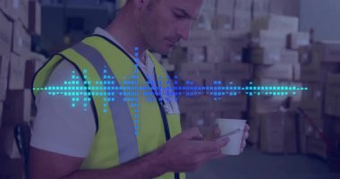 Depo çalışanı alarmı kontrol ediyor, elinde fincanla göğsünde dalga formu olan kameraya bakıyor. Güvenlik, yelek, sanayi, kutular, envanter, lojistik, verimlilik