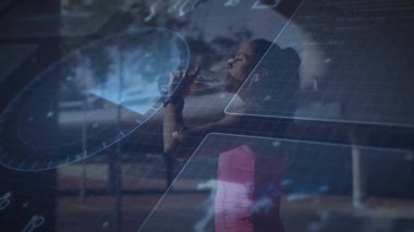 Cam duvarda duran, fitness seansını durduran, temiz şişe içen, HUD 'nin bilek verilerini takip eden bir kadın. Sporcu, hidrasyon, giyilebilir, stüdyo, gün ışığı, pencere, minimalist