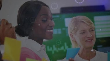 Başroldeki kadın elinde mavi notla iş planını cama yerleştiriyor, erkek katılıyor, insan kaynakları bağlanıyor. İşbirliği, beyin fırtınası, fikir, takım çalışması, ofis, modern ekran