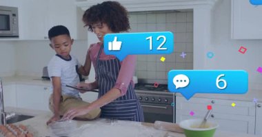 Anne oğluyla un karıştırırken tableti tıkırdatıyor. Aşçılık geri bildirimi yapan sosyal ikonlar gibi. Aile, bağ, mutfak, ev yemeği, dijital etkileşim, yetiştirme, yerli