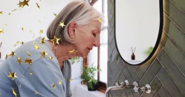 Kıdemli kadın musluk sapını değiştiriyor ve altın yıldızlı ellerle cilt kremi sürüyor. Kişisel bakım, hijyen, sağIık, cilt bakımları, zariflik, iç mekan, sükunet.