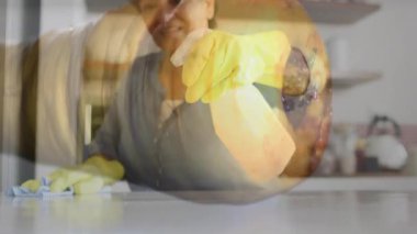 Senior woman pressing bottle nozzle, misting kitchen countertop and wiping with cloth to clean. Domestic, hygiene, sanitation, cleanliness, fresh, natural, detailed